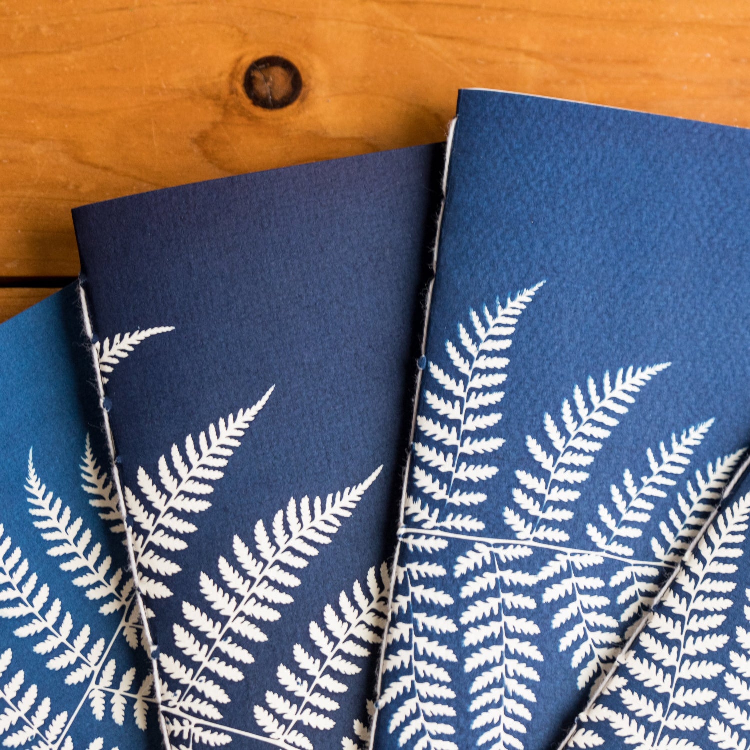 hand stitched, cyanotype notebooks with white fern patterns on a wooden surface