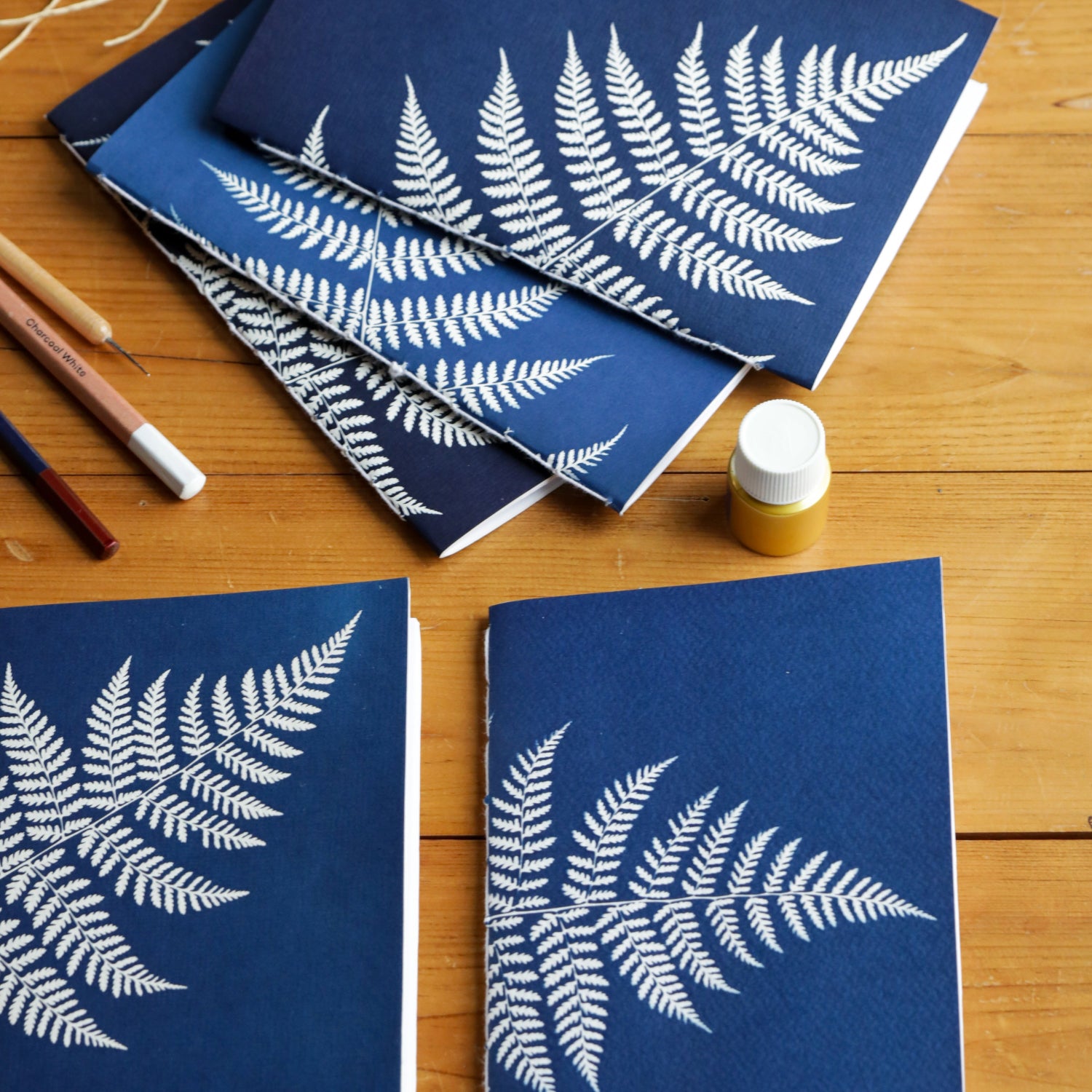 Blue notebooks with white fern patterns on a wooden surface