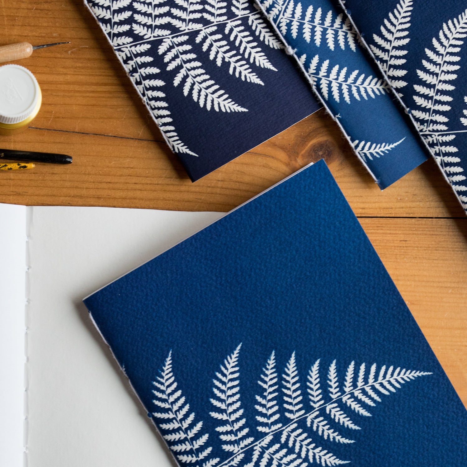 Blue notebooks with white fern patterns on a wooden surface, featuring the brand 'florigin'.
