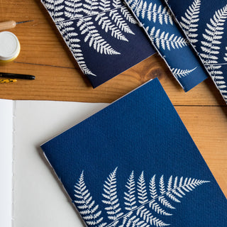 Blue notebooks with white fern patterns on a wooden surface, featuring the brand 'florigin'.
